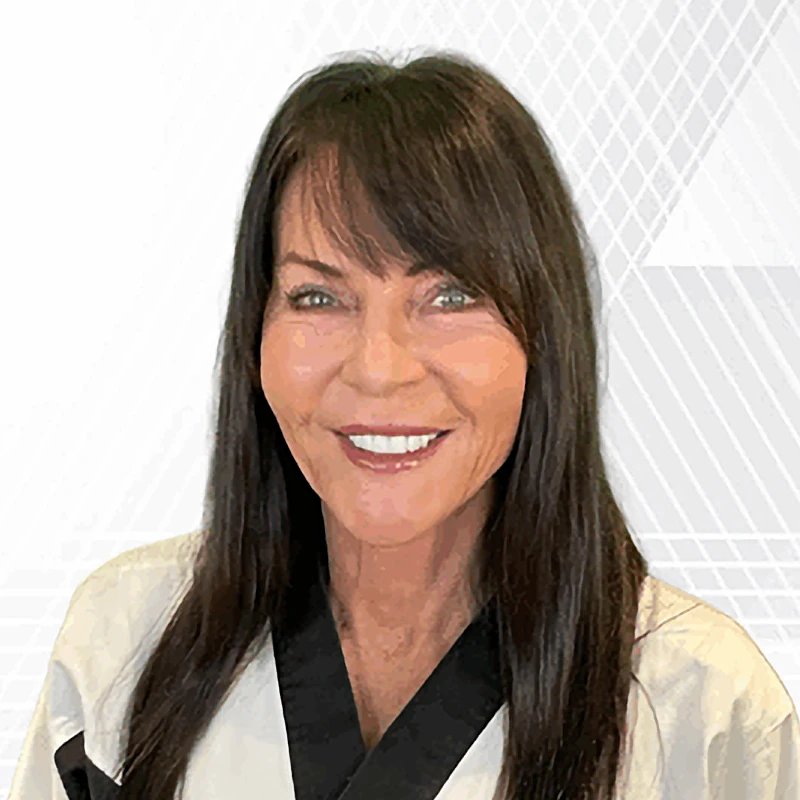 Sensei Jan Stockton smiles warmly for a professional headshot, wearing a white martial arts gi with black trim.