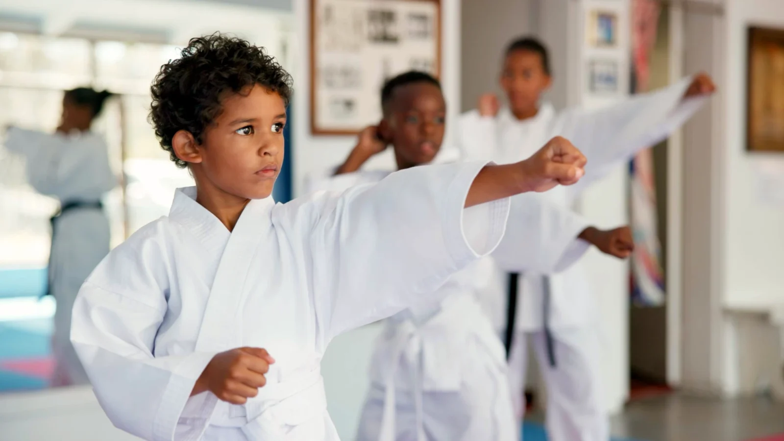 A focused boy leads a line of children in white karate uniforms practicing a powerful forward punch during class.