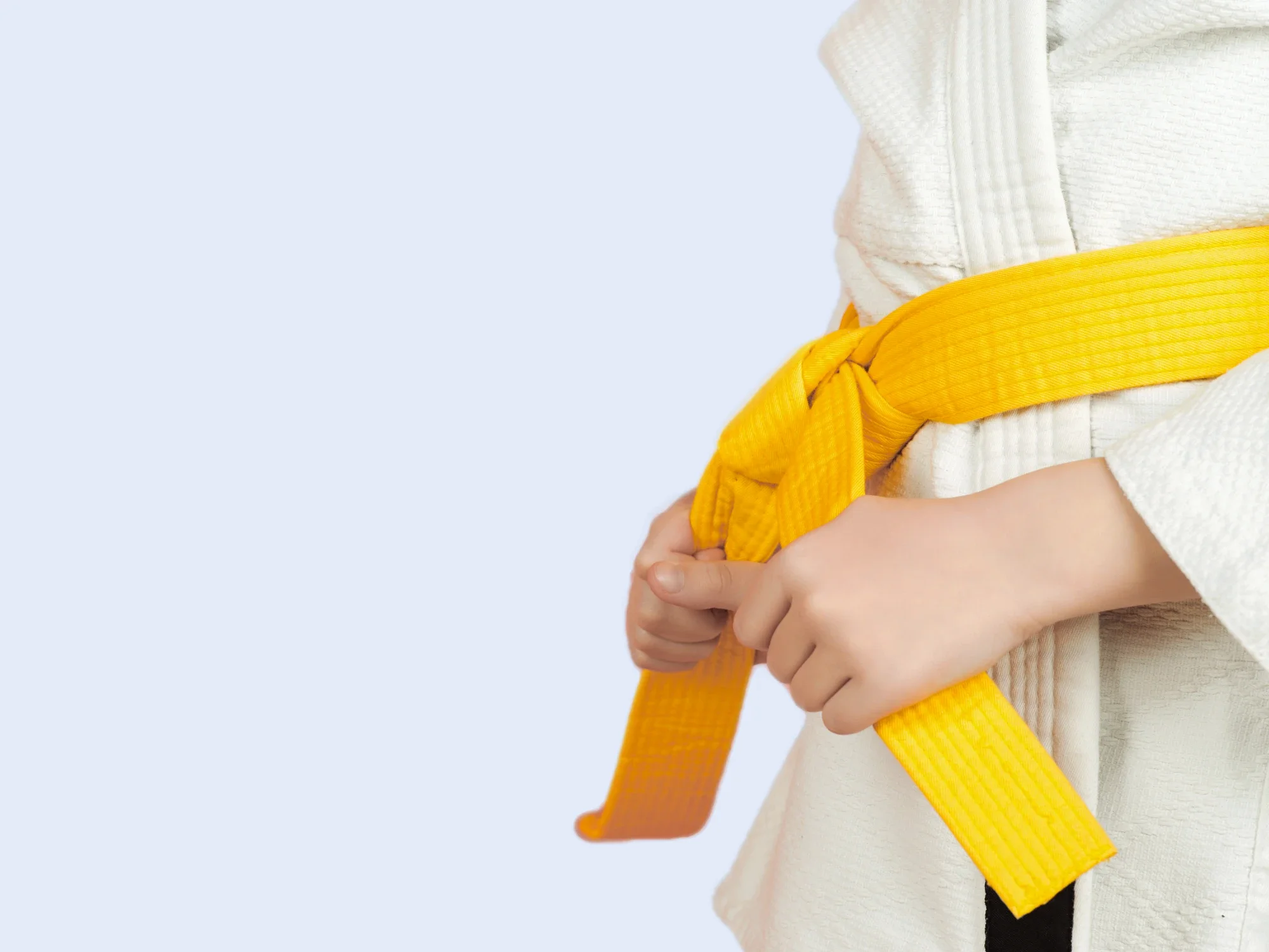 A martial arts student wearing a white uniform secures their bright yellow belt around their waist.